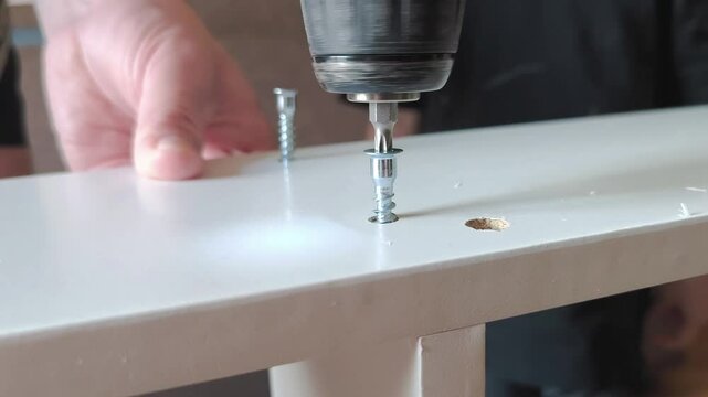Close-up of cordless screwdriver in action. Screw being driven into wooden surface. Male hand firmly holds tool. Sharp details, suitable for construction or home improvement themes.