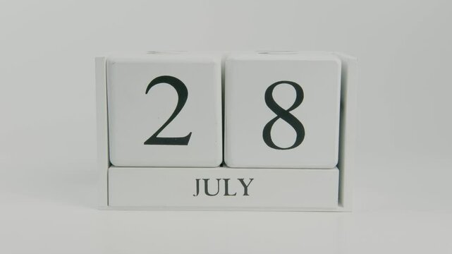 A hand flips a wooden calendar from July 28th to July 29th on a white background, symbolizing the progression of time