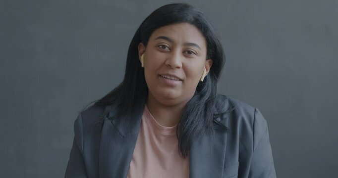 Portrait of cheerful young woman making online video call speaking and gesturing using wireless earphones looking at camera on black color background.