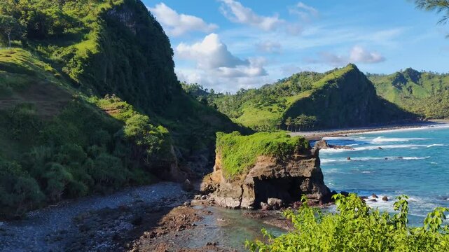 the beauty of the glamping ground panorama beside the blue ocean with large coral rocks that are hit by waves from the top of a high cliff. with rows of green mountains and blue skies