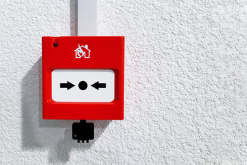 Wired fire alarm button on a textured plastered gray wall inside the building. Emergency button in...