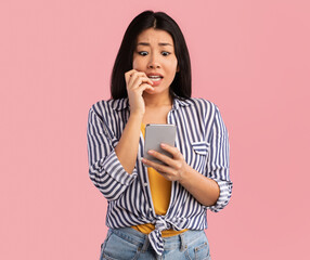 Portrait of anxious scared asian young woman looking at mobile phone seeing bad news, photos or...