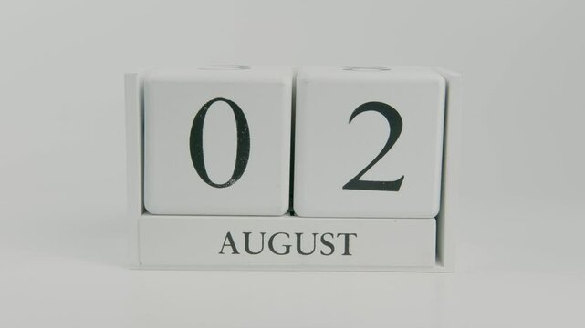 A hand flips a wooden calendar from August 2nd to August 3rd on a white background, marking the passage of time