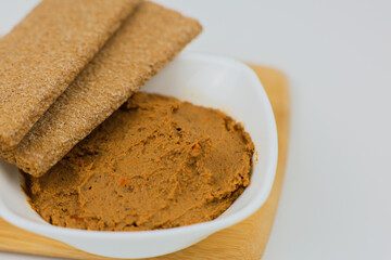 A close-up on a wooden board is a white plate with liver pate, slices of bread on top of it on a white background. The concept of healthy food, a healthy snack.