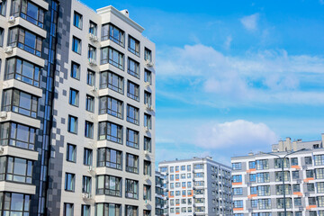 Fototapeta premium Multi-storey residential buildings of modern architecture with large windows and balconies against the background of the sky and clouds. 