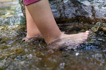 Toddler girl in nature with her feet in shallow stream water