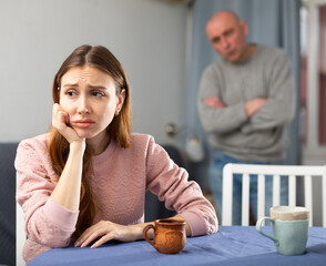 Portrait of a frustrated woman at the table, while disgruntled husband scolds her
