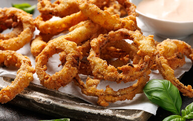 Deep fried onion rings on wooden board with sauce