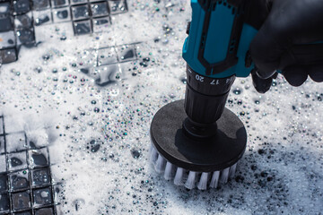 Close-up of an electric drill with a brush like attachment for cleaning a car rubber mat with soapy...