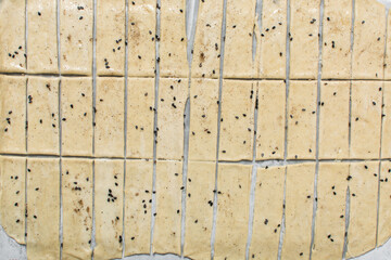 Overhead view of sliced sesame crackers dough on parchment paper, cutting cracker biscuit dough on...