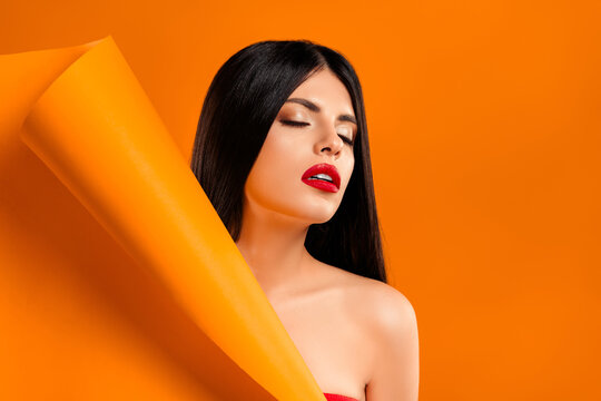 Beautiful young woman with red lips and brunette hair posing against a vibrant orange background