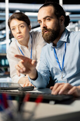Programmers in data center workplace using computer, verifying firewall configurations. Teamworking...