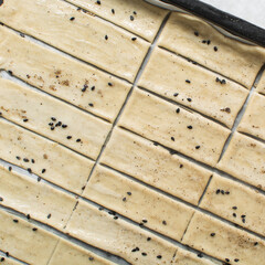 Overhead view of sliced sesame crackers dough on parchment paper, cutting cracker biscuit dough on...