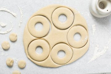 Overhead view of doughnut being cut out of dough, top view of doughnut dough on a white countertop,...