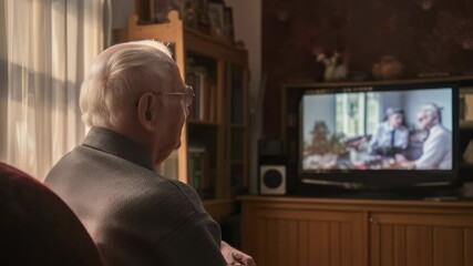 Elderly man sitting comfortably in an armchair, watching television in the living room, enjoying a peaceful afternoon at home while immersing himself in his favorite program
