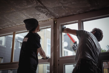 Two people are repairing a window, sealing the cracks with silicone.