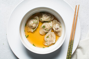 Overhead view of wonton soup in a white ceramic bowl, clear soup with dumplings in a white soup bowl