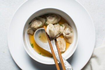 Overhead view of wontons in chopsticks, top view of soup wontons being eaten with chopsticks