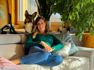 PORTRAIT, CLOSE UP: Playful shepherd dog lies wrapped around shoulders of a woman sitting on white...