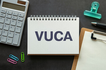 There is notebook with the word VUCA. It is an abbreviation for Volatility, Uncertainty, Complexity, Ambiguity as eye-catching image.