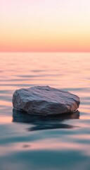 A solitary rock floats gently on a calm sea at sunrise.  Soft, pastel colors paint the sky and water