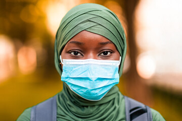 Outdoor portrait of african muslim woman in headscarf wearing protective medical mask on face for...