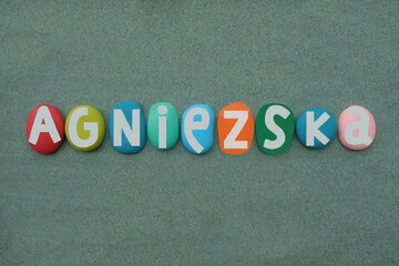 Agniezska, polish feminine given name composed with multi colored hand painted stone letters over green sand