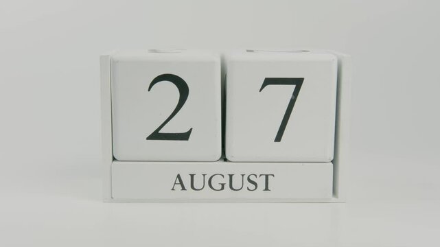 A hand flips a wooden calendar from August 27th to August 28th on a white background, signaling the change to a new day