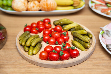 Fresh cherry tomatoes and pickles on tray. Round wooden serving tray filled with vibrant cherry tomatoes and crunchy pickles, ideal for healthy snacking or party platters.