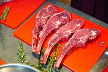 Raw tomahawk steaks with rosemary on board. Four raw tomahawk steaks arranged on a red cutting...