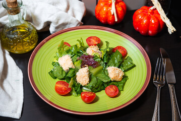 Fresh green salad with cherry tomatoes and cheese. Colorful salad with leafy greens, cherry tomatoes, and breaded cheese bites served on a vibrant plate with olive oil dressing.