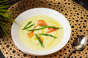 Creamy asparagus soup with smoked salmon. Gourmet bowl of creamy asparagus soup garnished with green asparagus spears, smoked salmon slices, and olive oil drizzle.