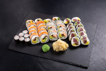 Assorted Sushi Platter with Rolls, Nigiri and Maki on Slate.
Variety sushi set including salmon rolls, tuna rolls, nigiri and maki, served with wasabi, ginger and soy sauce on black slate plate.
