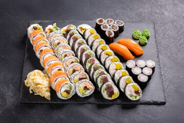 Assorted Sushi Platter with Rolls, Nigiri and Maki on Slate.
Variety sushi set including salmon rolls, tuna rolls, nigiri and maki, served with wasabi, ginger and soy sauce on black slate plate.
