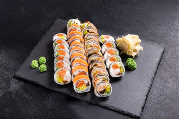 Assorted Sushi Platter with Rolls, Nigiri and Maki on Slate.
Variety sushi set including salmon rolls, tuna rolls, nigiri and maki, served with wasabi, ginger and soy sauce on black slate plate.