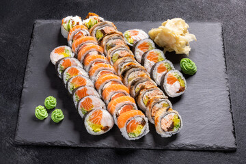 Assorted Sushi Platter with Rolls, Nigiri and Maki on Slate.
Variety sushi set including salmon rolls, tuna rolls, nigiri and maki, served with wasabi, ginger and soy sauce on black slate plate.