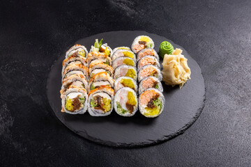 Assorted Sushi Platter with Rolls, Nigiri and Maki on Slate.
Variety sushi set including salmon rolls, tuna rolls, nigiri and maki, served with wasabi, ginger and soy sauce on black slate plate.