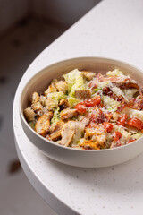 
Caesar Salad with Grilled Chicken, Parmesan and Croutons.
Classic Caesar salad featuring grilled chicken pieces, cherry tomatoes, croutons and grated Parmesan in a neutral bowl.