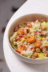 Caesar Salad with Grilled Shrimp, Croutons and Parmesan.
Fresh Caesar salad with grilled shrimp, cherry tomatoes, crunchy croutons and shredded Parmesan in a white bowl.