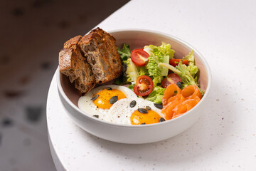 Breakfast Bowl with Eggs, Bacon, Salad and Bread.
Balanced breakfast bowl featuring sunny-side-up eggs, crispy bacon, fresh salad, cherry tomatoes, and rustic bread slices.