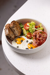 Breakfast Bowl with Eggs, Bacon, Salad and Bread.
Balanced breakfast bowl featuring sunny-side-up eggs, crispy bacon, fresh salad, cherry tomatoes, and rustic bread slices.