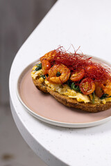 Open Sandwich with Scrambled Eggs, Shrimp and Chili Threads.
Gourmet toast topped with scrambled eggs, sautéed shrimp, spinach and red chili threads, served on a pastel plate.