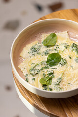 Spinach Ravioli with Creamy Parmesan Sauce.
Fresh ravioli pasta filled with spinach, topped with creamy cheese sauce and garnished with spinach leaves in a modern bowl.