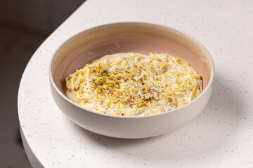 Creamy Pistachio Dessert Pasta.
Spaghetti in a smooth sweet cream sauce, topped with crushed pistachios, served in a ceramic bowl on a red background with floral decor.