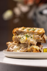 Grilled Tuna Melt Sandwich.
Toasted sandwich filled with baked tuna, melted cheese, and herbs, served with a pickle and dipping sauce on a ceramic plate.