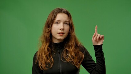 Teenage girl posing at camera pointing finger up, positive expression, isolated on chroma key green...