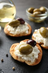 Delicious sandwiches with marinated olives, cream cheese and peppercorns on dark table, closeup