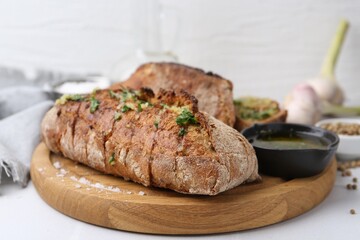 Tasty bread with garlic, herbs and oil on white table, closeup