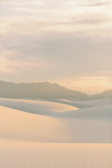 Soft golden light casting shadows over smooth dunes with distant mountains at sunset