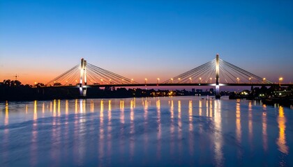 Fototapeta premium Illuminated cable-stayed bridge over calm river at twilight. Serene cityscape reflected in water.